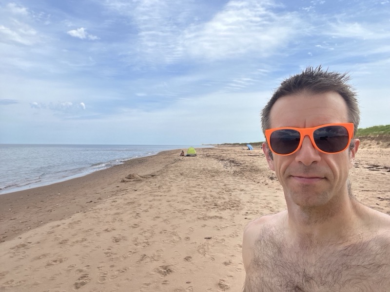 Beach selfie with orange sunglasses and tents in the distance
